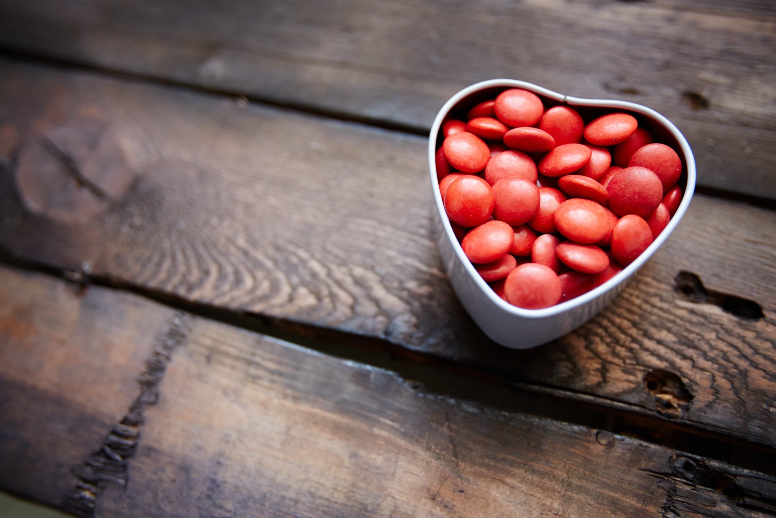 Red small candies in heart shaped box against wooden background