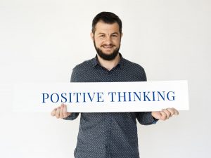 man holding a sign that says positive thinking