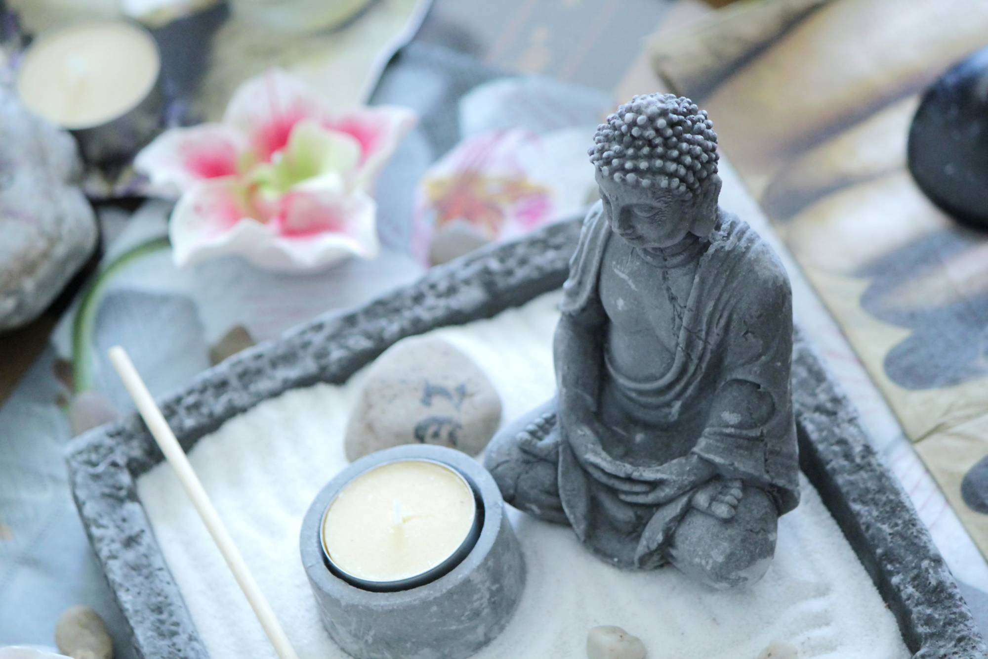 Grey stone buddha in front of a small yellow candle on a zen table